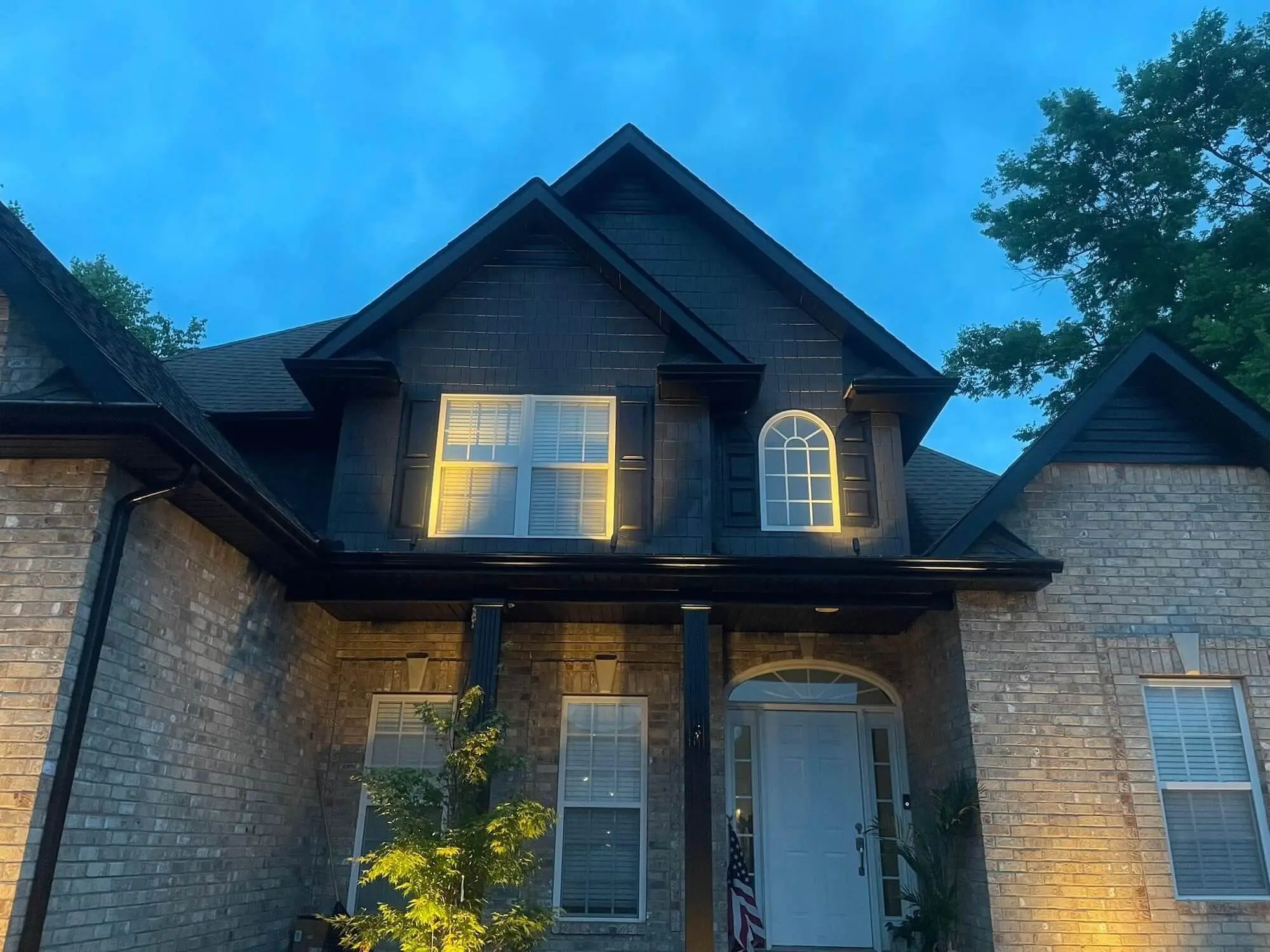 Two-story brick home with dark painted exterior trim, gables, and warmly lit windows at dusk in Brentwood, TN